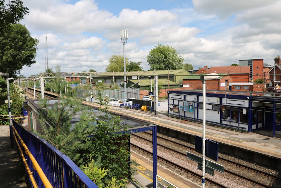 A narrow railway platform next to curved train tracks with a yellowed safety line along the edge. The platform surface features textured paving slabs and a yellow tactile strip near the edge for visua